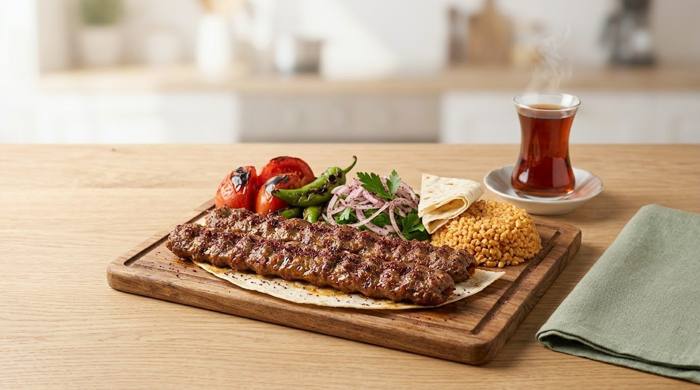 Ahşap servis tahtasında lavaş üzerinde Adana kebap, közlenmiş domates ve biber